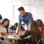 male high school teacher standing by student 3QRW2KP - DIGITOK